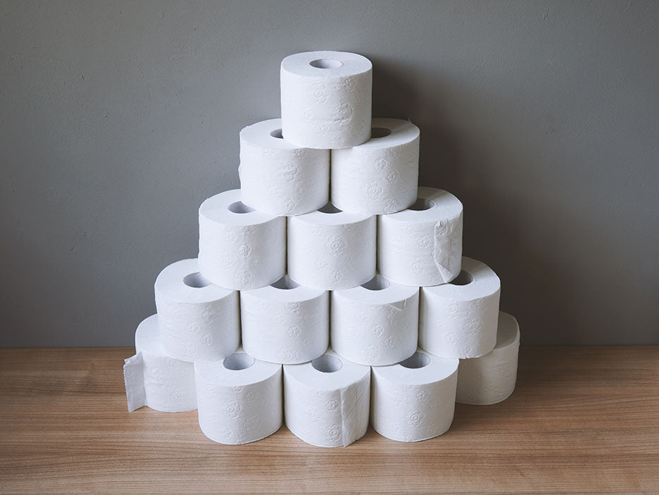 Toiletpapir stablet oven på hinanden foran grå væk i en pyramide form